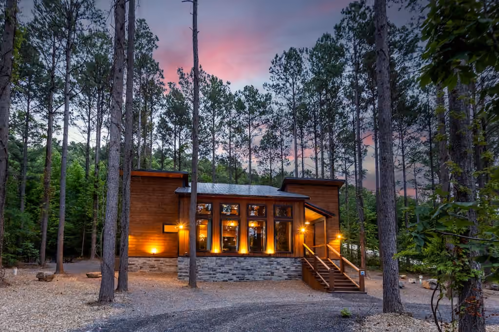 A modern cabin glowing among tall pine trees at twilight